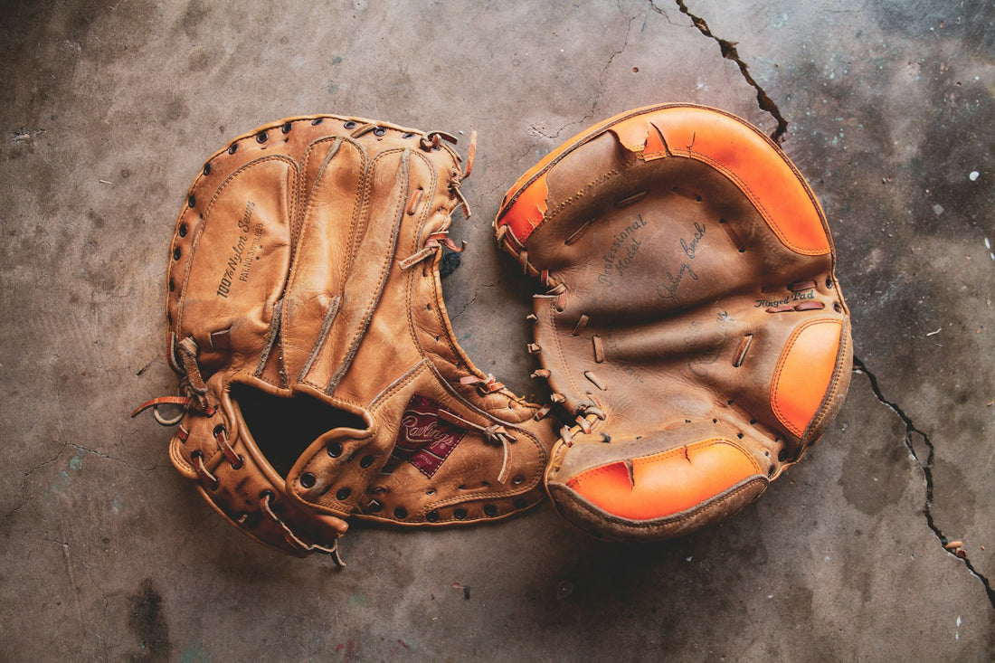 Two leather baseball gloves are shown on the ground, demonstrating the importance of leather conditioners.