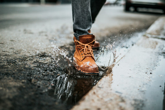 A person in leather boots steps in a puddle, demonstrating importance of waterproofing leather.