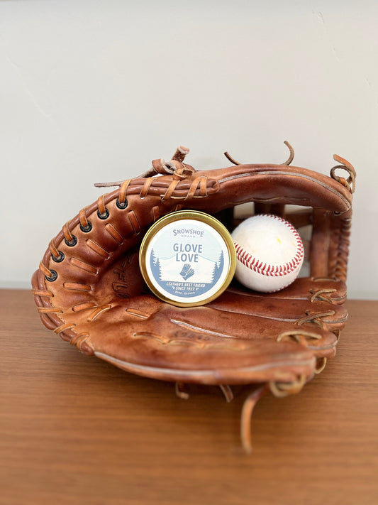 Baseball glove with a baseball and a container labeled 'Glove Love' on a wooden surface.