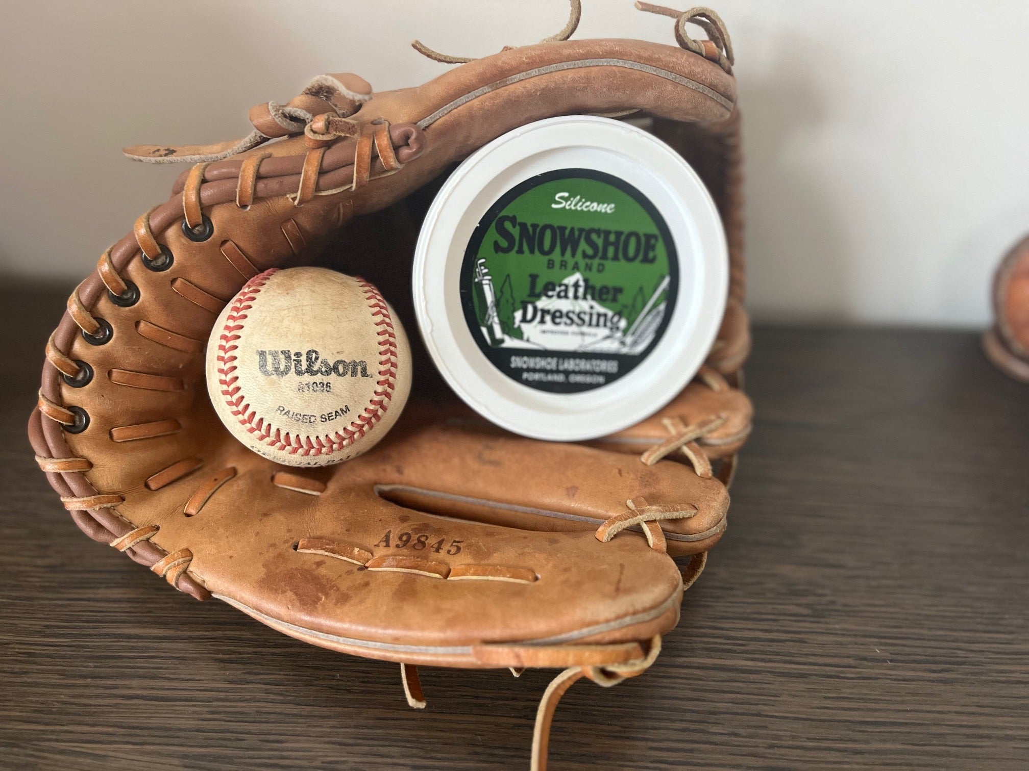 Photograph of a baseball mitt and Wilson baseball with 8oz tub of Snowshoe Leather Dressing in Mitt 