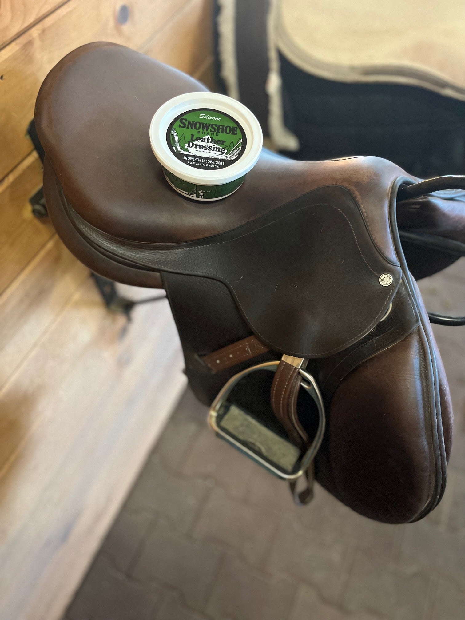 A tub of Snowshoe Brand Leather Conditioner is sitting on top of horse tack.