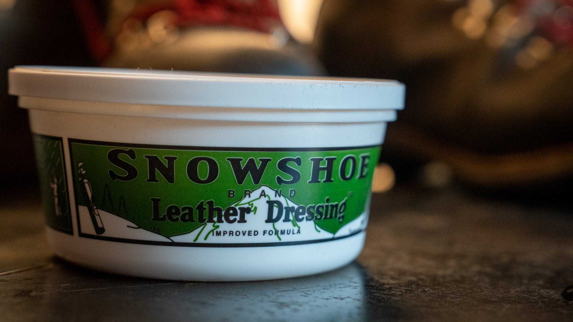 A close up photo of an 8oz tub of Snowshoe Brand Leather Conditioner is displayed on a table. 