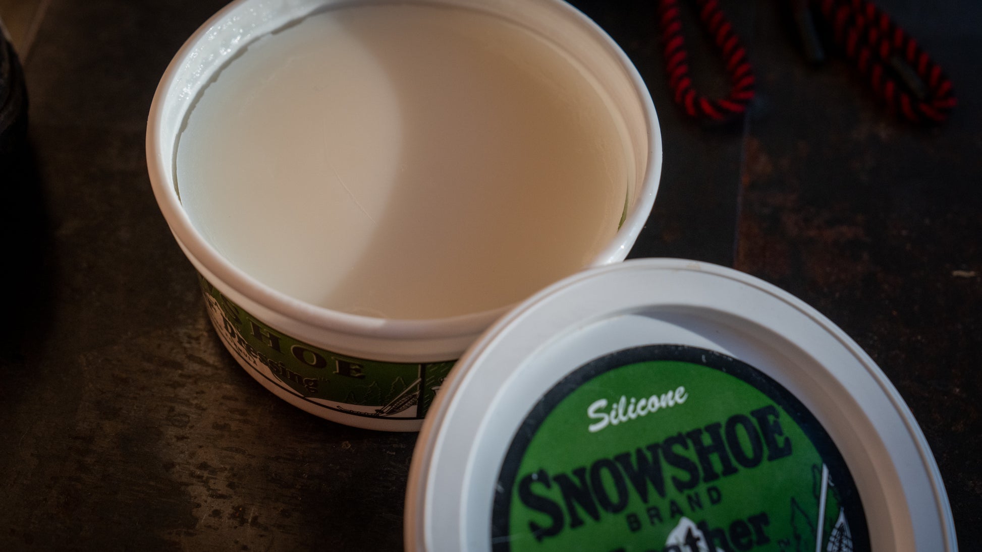 An 8oz tub of Snowshoe Brand Leather conditioner is displayed with its lid off. 